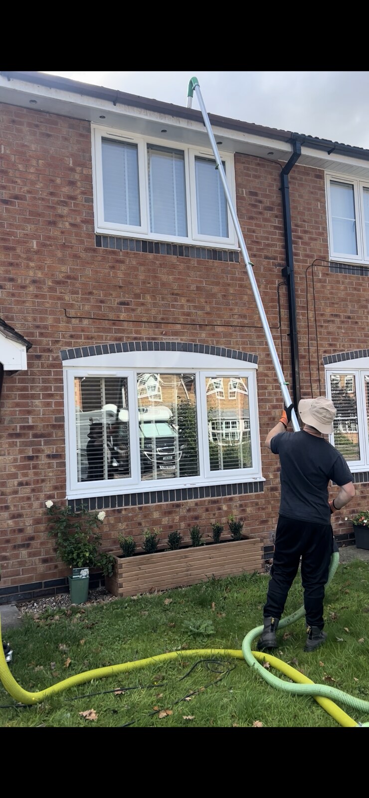 Gutter clearing with reach-and-wash pole on a brick house
